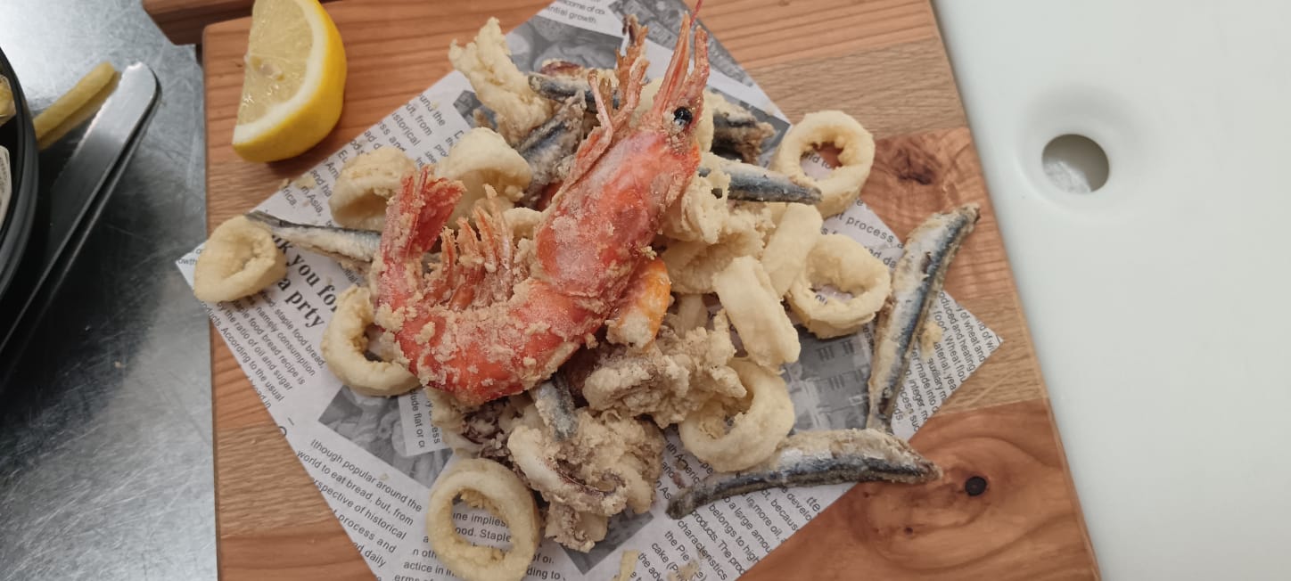 Frittura mista di pesce dorata e croccante servita su carta paglia con gamberone, calamari, alici e limone