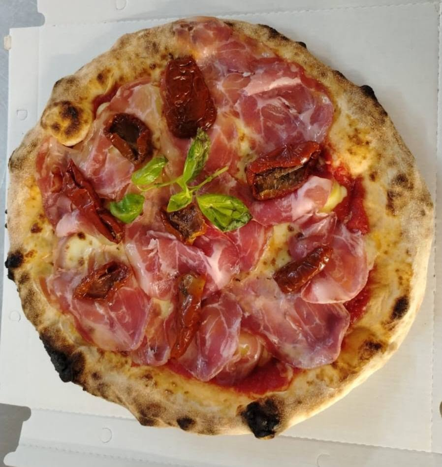 Pizza con fette di capocollo nostrano, pomodori secchi sott'olio e basilico fresco