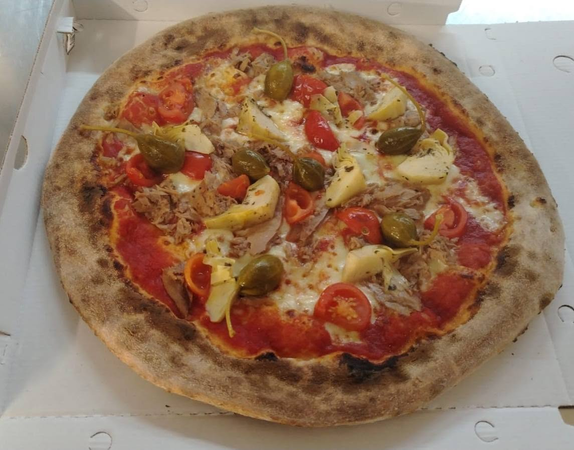 Pizza ricca con pomodoro, filetti di tonno, cuori di carciofo, pomodorini e capperi con gambo